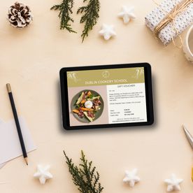 Dublin Cookery School digital gift voucher displayed on a tablet surrounded by Christmas decorations and wrapping materials.