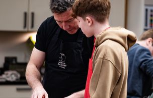 Chef instructor guiding a teenage student during a practical cooking session in a teaching kitchen.