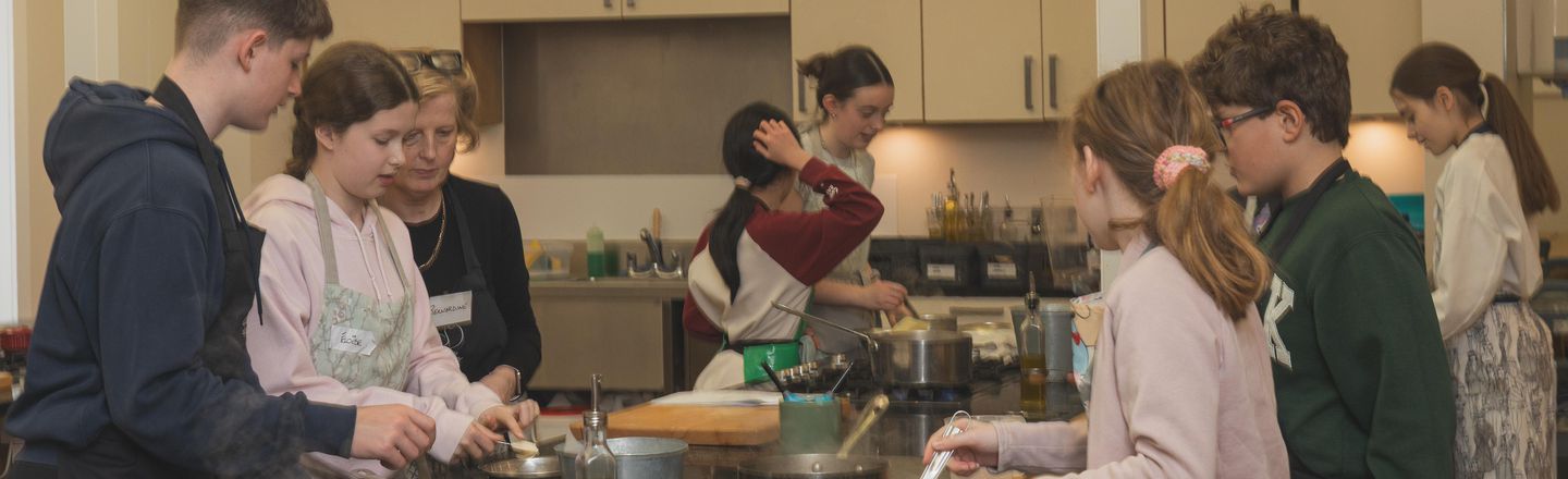 Teenagers and a tutor cooking together at the hob during a Senior Growing Gourmets summer camp at Dublin Cookery School, Blackrock