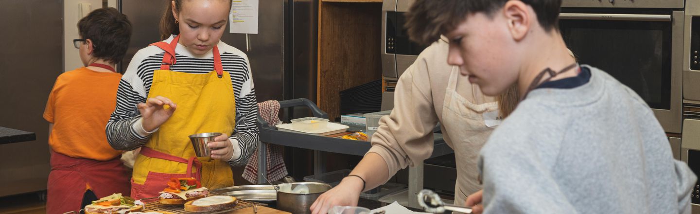 Teenagers cooking at Dublin Cookery School during a Junior Growing Gourmets summer camp, working at kitchen benches with fresh ingredients and recipe notes