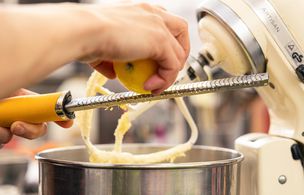 Cooking class in a teaching kitchen, with an instructor and students preparing food at workstations.