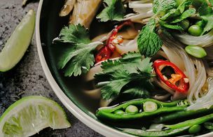 Bowl of Vietnamese-style rice-noodle soup with fresh coriander, mint, red chilli and lime wedges