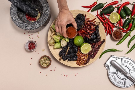 Overhead flat-lay of dried chillies, whole spices, limes and ground paprika arranged on a wooden board with a mortar and pestle, used in a Dublin Cookery School class on creative cooking with spices.