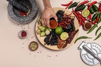 Overhead flat-lay of dried chillies, whole spices, limes and ground paprika arranged on a wooden board with a mortar and pestle, used in a Dublin Cookery School class on creative cooking with spices.