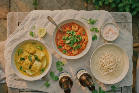 Three summer curry dishes — golden fish curry with lime, prawn curry with coriander, cashew noodle curry — served with cold beer on a linen cloth at Dublin Cookery School's Summer Curries and Beer class