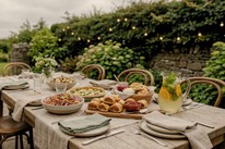 A summer garden party spread on an outdoor table at Dublin Cookery School in Blackrock: rainbow slaw, a spinach and feta tart, sausage rolls with tomato relish, and a jug of herb-and-citrus mocktail.