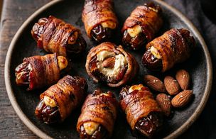 Nine bacon-wrapped Medjool dates with halloumi and smoked almonds on a dark plate, one broken open to show the mascarpone and almond filling inside. Dublin Cookery School recipe.