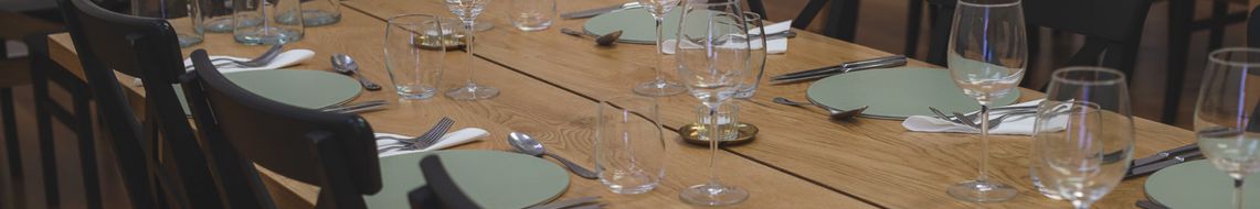 A long oak dining table set for a formal meal, with sage green placemats, folded white napkins, polished cutlery and tall wine glasses arranged at each place setting.