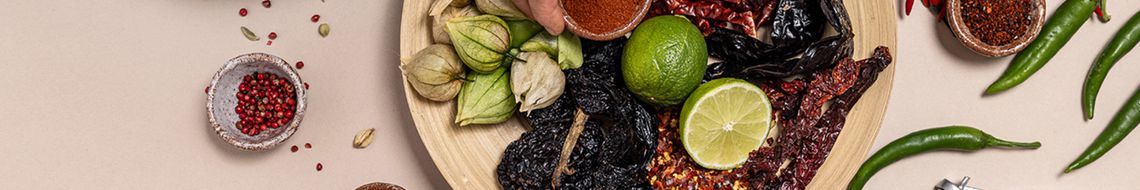 Wide crop of a spice and dried chilli flat-lay including limes, cardamom pods and chilli flakes, illustrating the building blocks of flavour-led cooking at Dublin Cookery School.