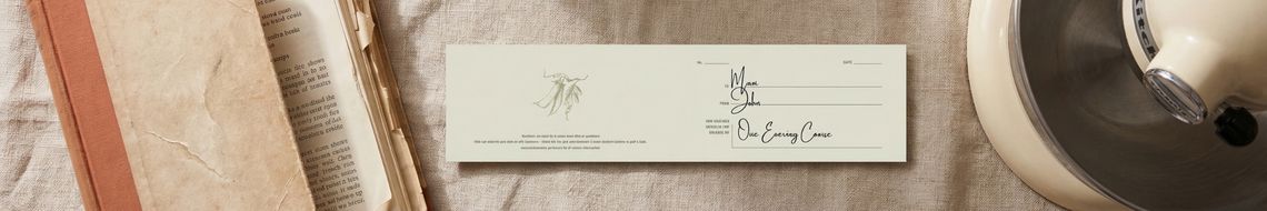 A Dublin Cookery School gift voucher sits on a warm linen surface alongside a hardback cookbook with a worn spine, and a KitchenAid Stand Mixer partially in frame at the edge.