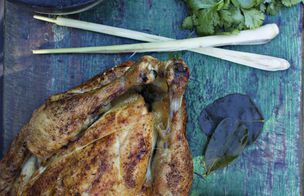 Roast chicken legs with spring onions and herbs on a blue surface.