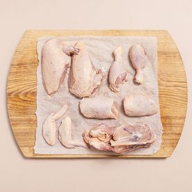 A whole chicken broken down into breasts, thighs, wings and carcass laid out on parchment paper on a wooden board, demonstrating how to get more meals from a single bird.
