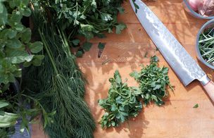 Delicate herbs freshly chopped on a chopping board with chefs knife lying alongside