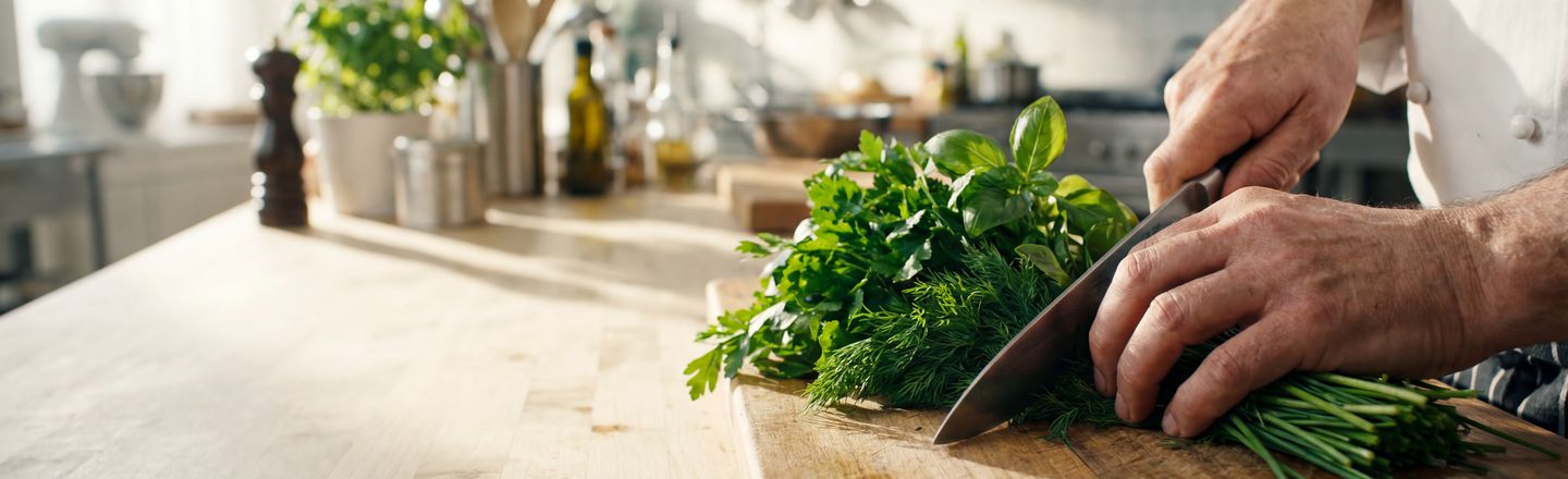 Close-up of hands demonstrating precision knife work at Dublin Cookery School, chopping fresh herbs on a wooden worktop.