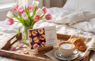 Dublin Cookery School gift voucher displayed on a wooden breakfast tray alongside fresh tulips, coffee, and a croissant, representing the gift of a lifelong skill.
