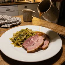 A plate of sliced boiled bacon with braised green cabbage on a white dinner plate, photographed in a warmly lit home kitchen as a hand pours amber whiskey caramel sauce from a ceramic jug over the dish, a tea towel and mug visible in the background.
