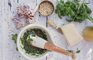 Fresh basil pesto being ground by hand in a mortar and pestle, with garlic, pine nuts and Parmesan
