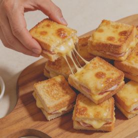 Bite-sized mini croque monsieur sandwiches with melted cheese on a wooden sharing board. An inexpensive party finger food idea for Six Nations Super Saturday.