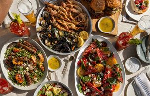 A full summer BBQ table spread — grilled prawns, mussels, sausages, watermelon salad, burgers, tropical fruit and cocktails — representing the kind of menu covered in Dublin Cookery School's summer BBQ masterclasses