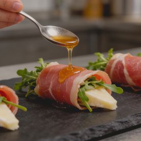 Parma ham canapé rollups with Taleggio cheese and fresh rocket being drizzled with honey. A cheap party food option that maintains a premium aesthetic.