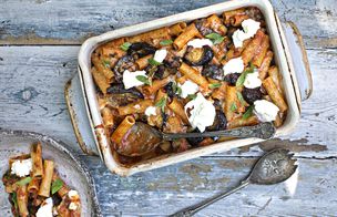 A group of students in black aprons collaborating over a steaming pot during a hands-on cookery class, listening to instruction in a busy kitchen environment.