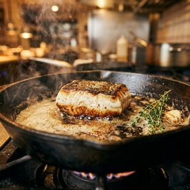 Monkfish medallion searing in a cast iron pan with foaming butter and thyme — how to cook monkfish at home