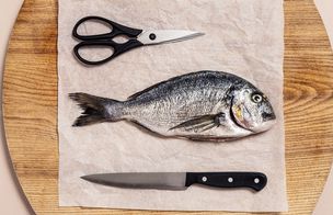 A whole sea bream on baking paper on a wooden board, with kitchen scissors and a chef's knife laid either side, ready to be prepared at Dublin Cookery School.