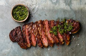 Slices of medium-rare steak fanned out on a grey stone board beside a small bowl of green chimichurri — from the Steaks, Sauces & Sides class at Dublin Cookery School.