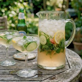 A jug of non-alcoholic herb-and-citrus mocktail with mint, lemon and ice on a garden table, served in real glasses — non-alcoholic drink ideas from Dublin Cookery School.